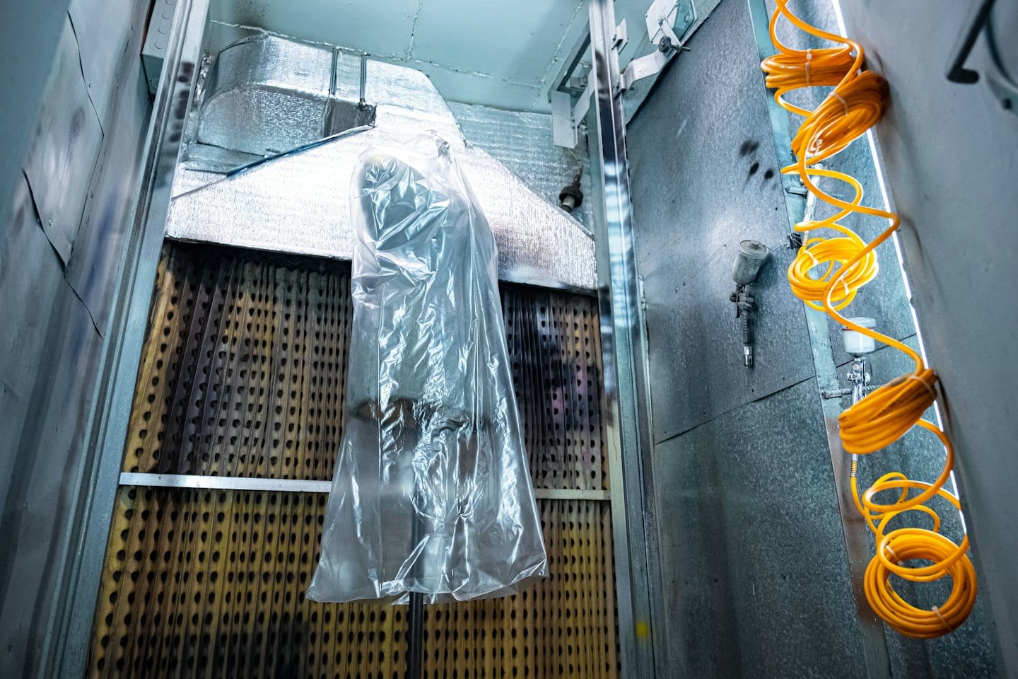 Industrial paint booth with hanging object and spray equipment.