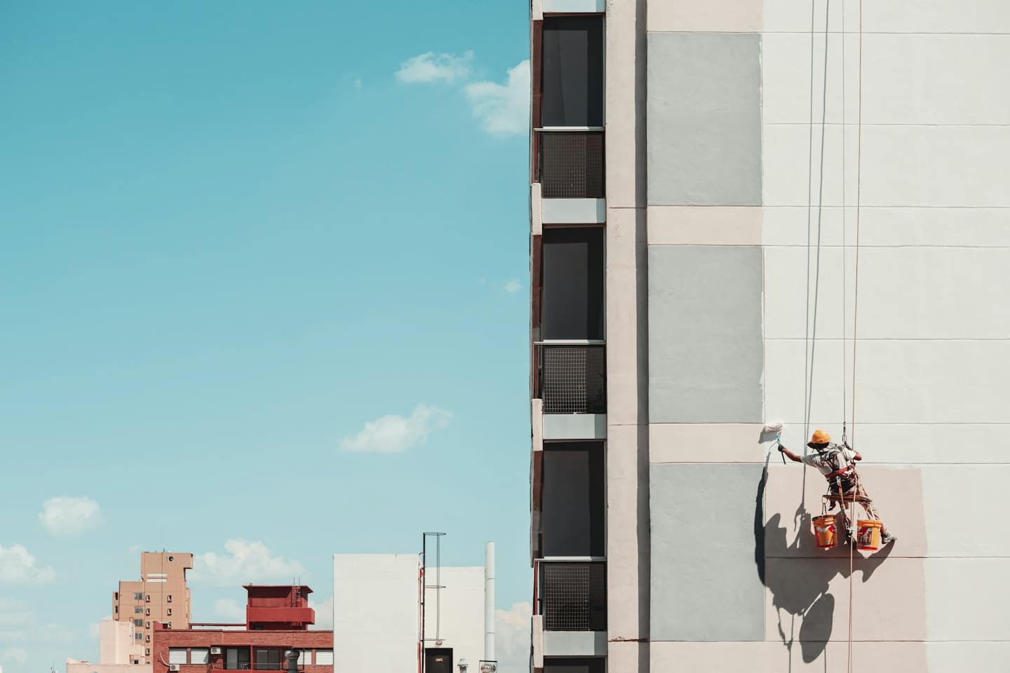 Worker suspended by ropes paints exterior of modern building.